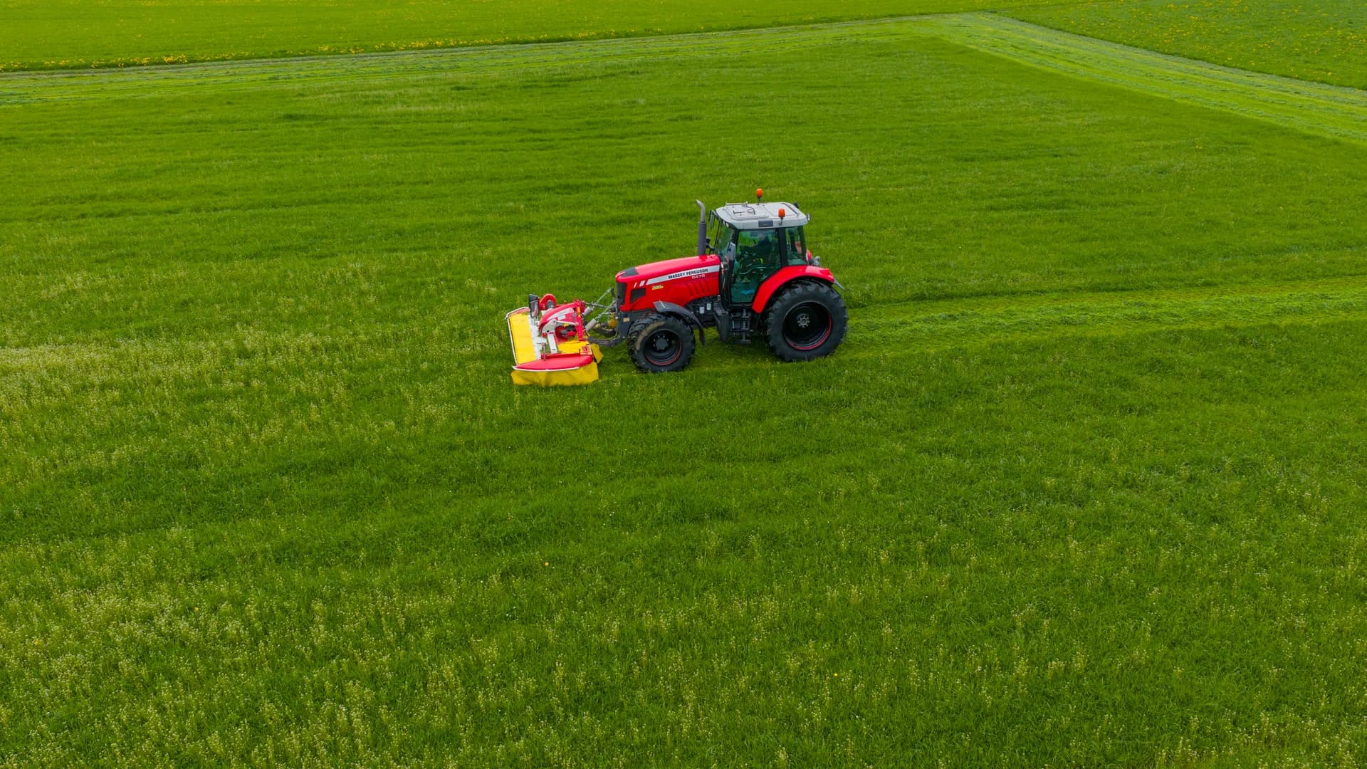 Tracteur rouge fauchant une prairie, vue drone